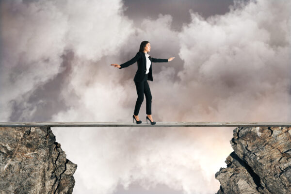 Young businesswoman balancing between two cliffs on cloudy sky background. Equilibrium concept